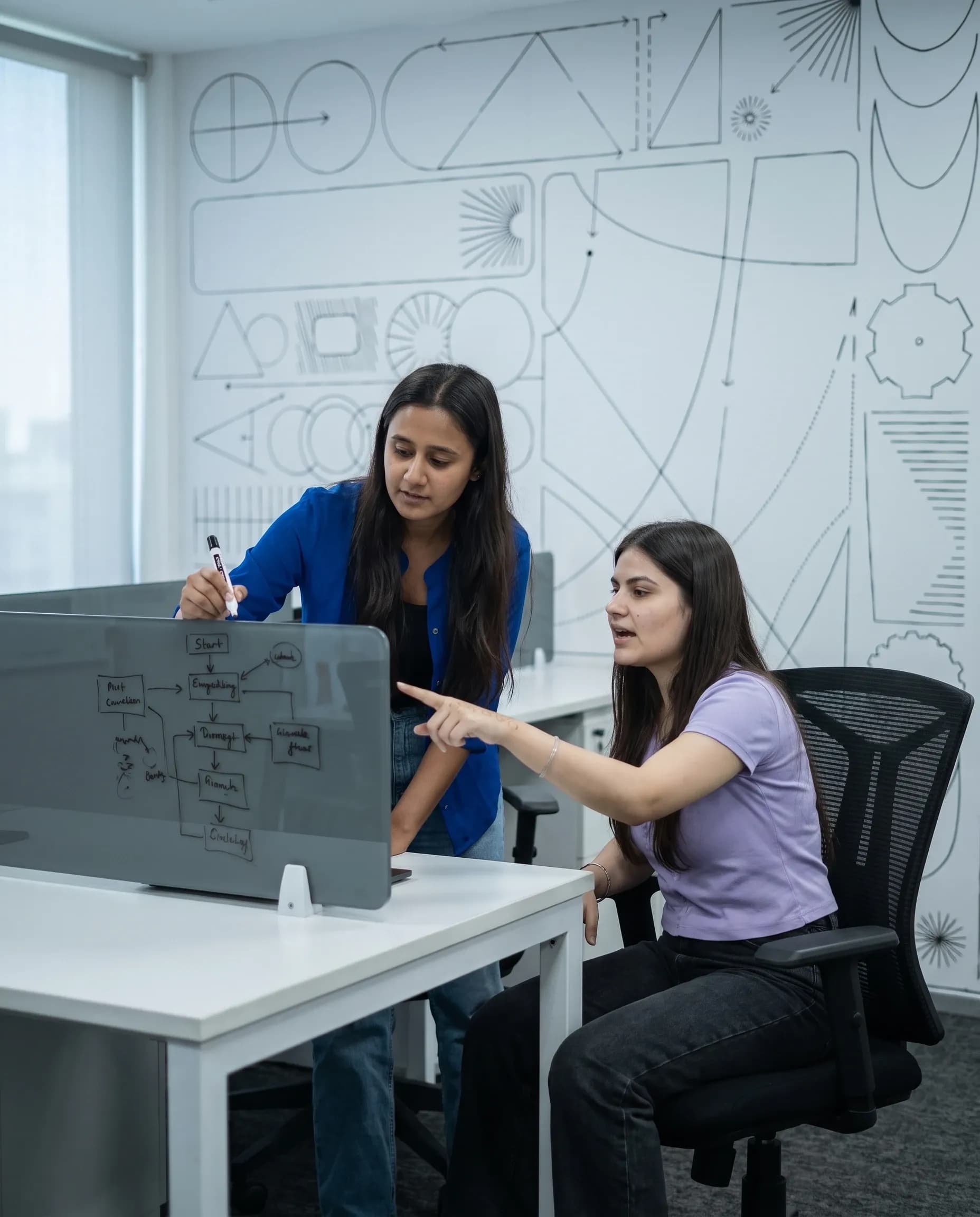 Two DigiIQ engineers sketching a flowchart on a glass desk partition